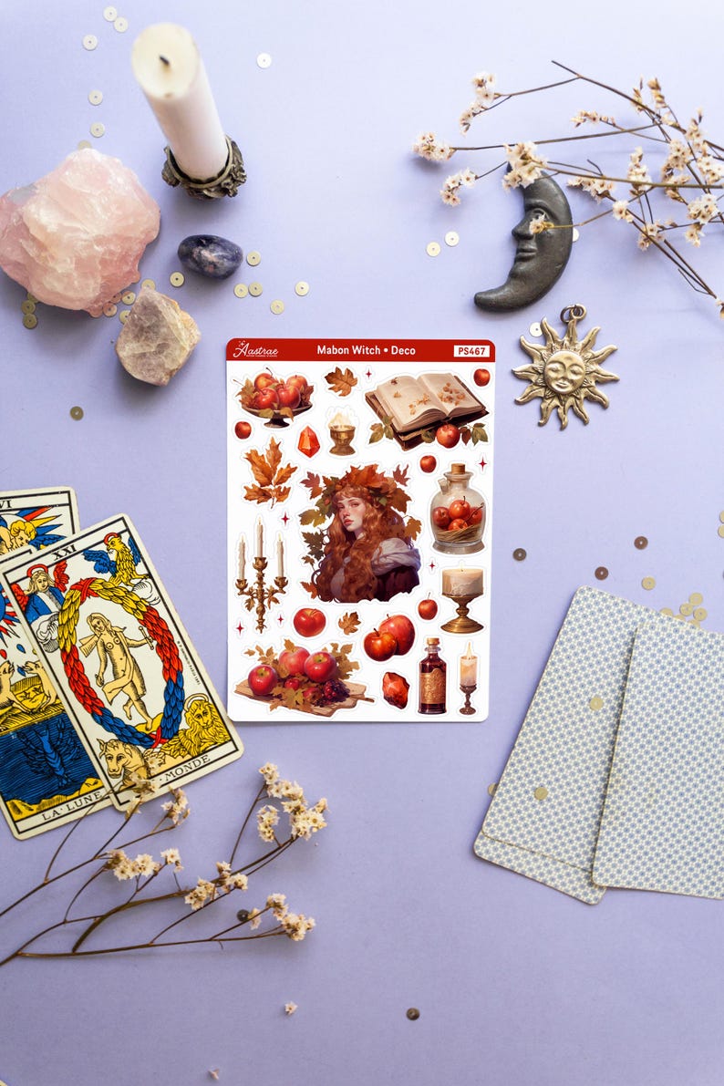 May include: A sheet of stickers featuring a witch with red hair and a crown of leaves, surrounded by apples, candles, and other autumnal imagery. The sticker sheet is titled "Mabon Witch + Deco" and has the number "PS467" printed on it.
