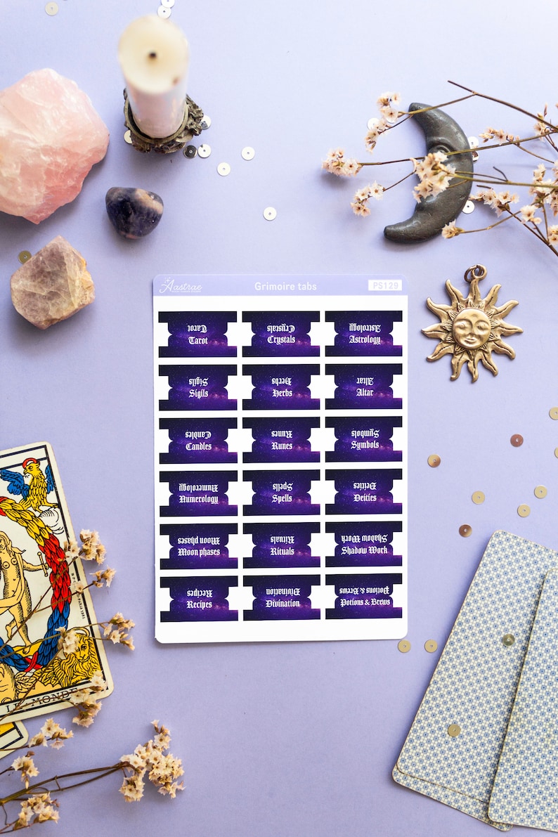 May include: A set of 18 purple and black planner stickers with a galaxy background. The stickers are labeled with various topics related to witchcraft, such as tarot, crystals, astrology, sigils, herbs, altar, candles, runes, symbols, numerology, spells, deities, moon phases, rituals, shadow work, recipes, divination, and potions & brews.