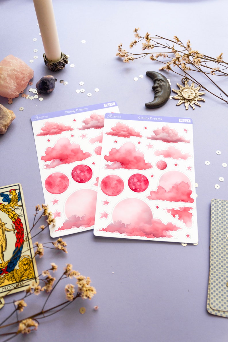 May include: Two sheets of pink and white stickers with a watercolor design of clouds, stars, and moons. The stickers are labeled "Cloudy Dreams" and have the product number "PS327".