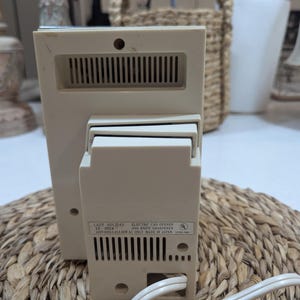 May include: A beige electric can opener and knife sharpener with a white power cord. The back label reads: LADY HOLIDAY 10-0024 ELECTRIC CAN OPENER AND KNIFE SHARPENER 120V 60Hz 1.45A 90W AC ONLY MADE IN JAPAN. The device features ventilation slots.