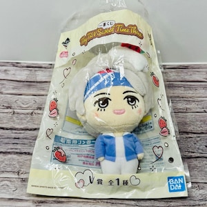 May include: A plush doll of a character from the "Tiny Tay Sweet Time Theme" series, packaged in a clear plastic bag. The doll has a light blue jacket, white shirt, and a blue and white headband. The packaging includes text and strawberry illustrations.