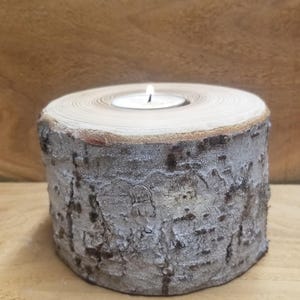 May include: A wooden candle holder shaped like a tree stump with a small white tea light candle in the center.