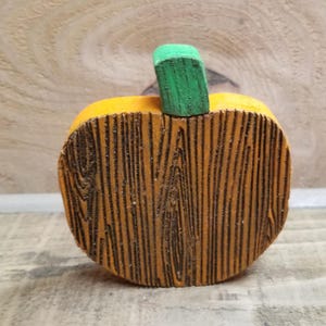 May include: A wooden pumpkin with a green stem. The pumpkin is painted orange and has a wood grain texture.