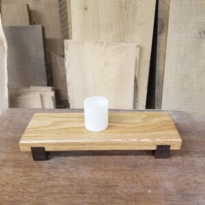 May include: A wooden candle holder with dark brown accents and a white candle on top. The holder is sitting on a wooden surface.