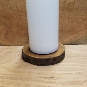 Op de afbeelding: Witte pilaarvormige kaars met een golvende bovenkant, die op een ronde houten schijf staat.