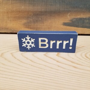 May include: A blue wooden sign with a white snowflake and the text "Brrr!" in white.