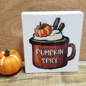 May include: White wooden sign with a hand-painted image of a brown mug with whipped cream and a pumpkin on top. The mug says "Pumpkin Spice" in brown letters.