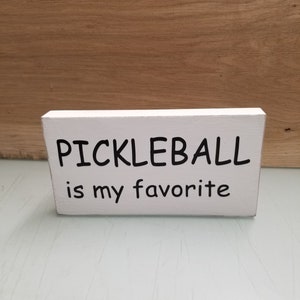 May include: White wooden sign with black text that reads "Pickleball is my favorite".