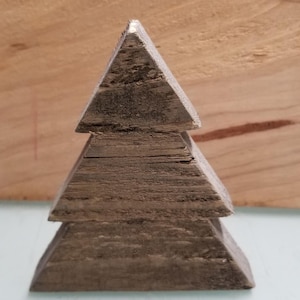 Puede incluir: Un adorno de árbol de Navidad de madera hecho de tres piezas triangulares de madera apiladas. La madera es de color marrón oscuro y tiene un aspecto rústico.