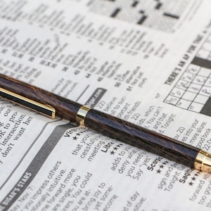 PEN110 - Un elegante bolígrafo tipo portafolios de estilo delgado con detalles dorados, madera de wengué con vetas distintivas y acabado con pegamento CA pulido.