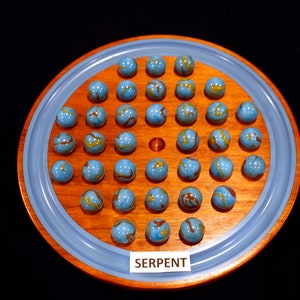 May include: A wooden game board with a blue rim and a circular wooden playing surface. The board is filled with blue marbles with gold swirls. The board has a label that reads "SERPENT".
