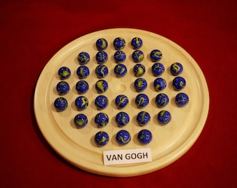 Puede incluir: Un tablero de juego de madera con 37 canicas azules y amarillas dispuestas en un patrón circular. El tablero tiene una etiqueta que dice "VAN GOGH".