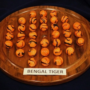 May include: A wooden game board with 33 orange and black marbles arranged in a circle. The board has the words "Bengal Tiger" printed on a label.