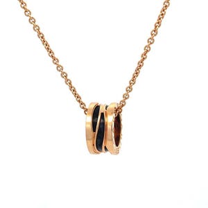 May include: A rose gold necklace featuring a cylindrical pendant with a central black ceramic band. The pendant is suspended from a delicate rose gold chain. The design incorporates metallic rose gold edges flanking the dark center section.