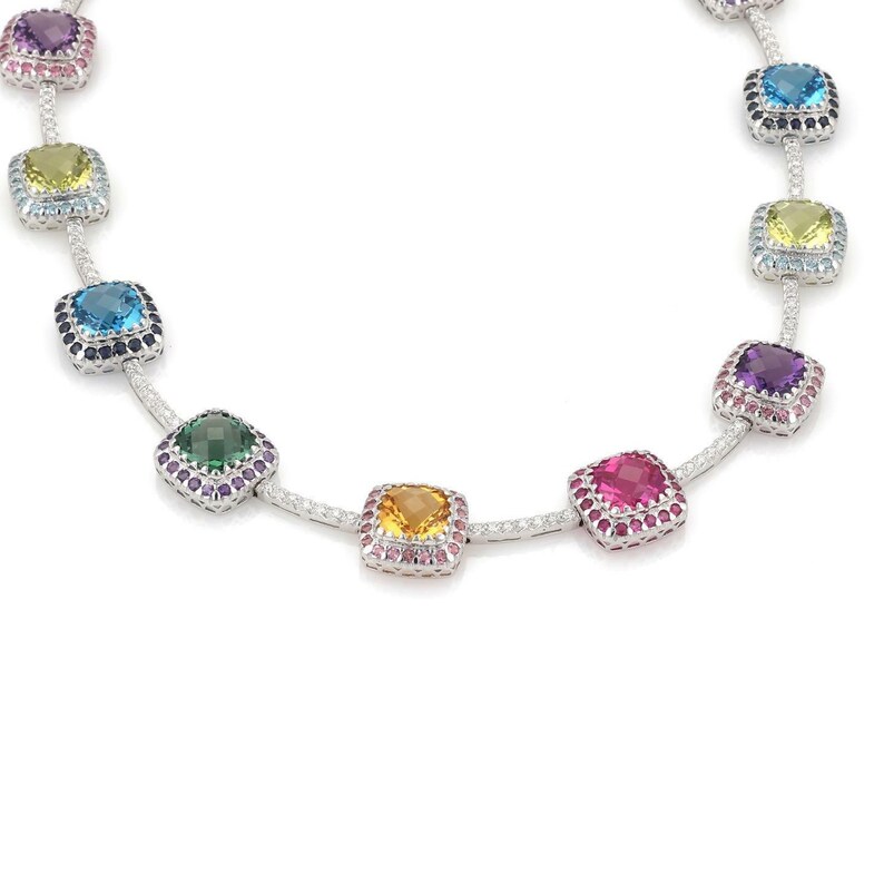 May include: A silver necklace featuring a series of square-cut gemstones in various colors, including purple, yellow, blue, green, orange, and pink. Each gemstone is surrounded by smaller, accent stones. The necklace is displayed against a white background.
