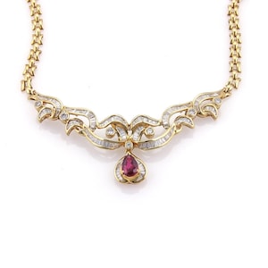 May include: A gold necklace with a pendant featuring a pear-shaped ruby. The necklace has a decorative design with baguette and round-cut diamonds. The chain is a linked design.