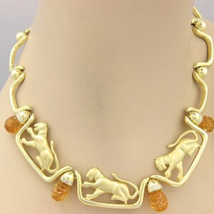 May include: A gold-toned necklace featuring stylized lion figures within rectangular frames. The necklace has amber-colored accents and small diamond embellishments. The design is set against a neutral background, highlighting the jewelry's intricate details.