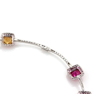 May include: A silver bracelet with square-cut gemstones in shades of yellow, pink, and green. The gemstones are set in a silver frame with small, clear stones around the edges. The bracelet is on a white background.