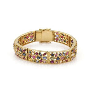 May include: A gold bracelet with a floral filigree design. The bracelet is adorned with a variety of colorful gemstones, including red, blue, pink, and white stones. The bracelet is rectangular in shape and has a clasp closure.