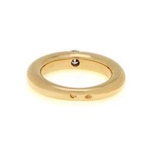 May include: A gold band ring with a single, small, round, clear diamond set in the center of the band. The ring is smooth and has a slightly rounded shape.