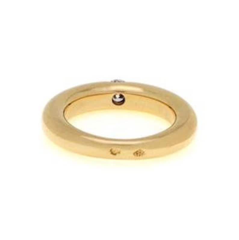 May include: A gold band ring with a single, small, round, clear diamond set in the center of the band. The ring is smooth and has a slightly rounded shape.