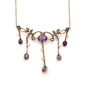 May include: A gold-toned necklace featuring an oval amethyst center stone and dangling amethyst pendants. The necklace is adorned with small pearls and decorative flourishes, creating an elegant and vintage aesthetic.