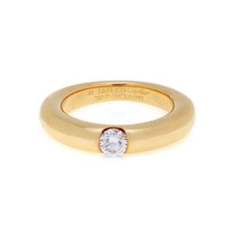 May include: A gold band ring with a single round diamond set in the center. The ring is inscribed with '17 5088 93 Cartier 1993'.
