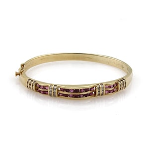 May include: A gold bangle bracelet with three rows of pink gemstones and small white gemstones. The bracelet has a clasp closure and is set against a white background.