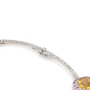 May include: A silver necklace with a clasp, featuring a large, faceted, yellow gemstone surrounded by small pink gemstones. The necklace is set with numerous small, clear gemstones.