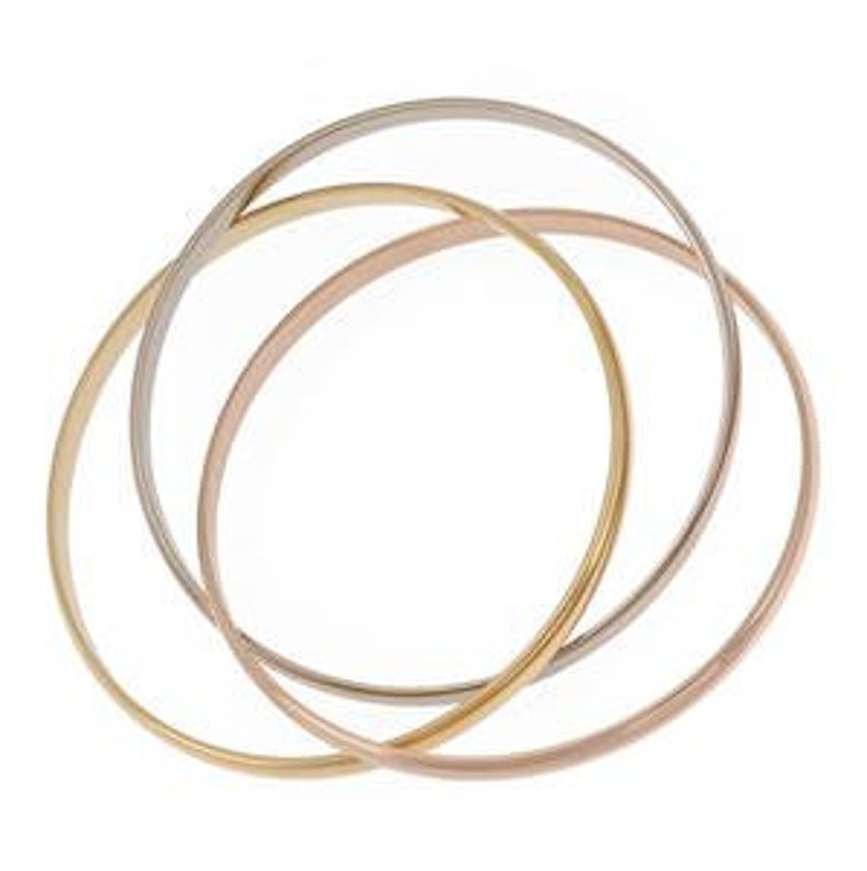 May include: Three interlocking gold bangles. The bangles are in different shades of gold: yellow, rose, and white. The bangles are stacked on top of each other, with the yellow gold bangle on the bottom, the rose gold bangle in the middle, and the white gold bangle on top.