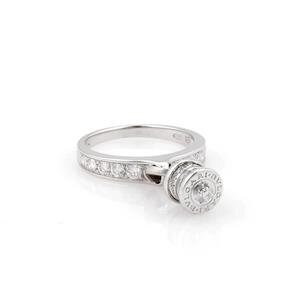 May include: A silver ring with a round, rotating centerpiece. The band is encrusted with small, clear stones. The centerpiece features a circular design with a central stone and engraved details. The ring is set against a white background.