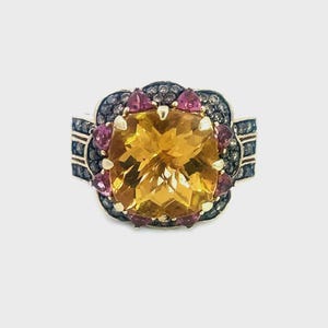 May include: A gold ring featuring a large, square-cut, yellow gemstone at the center, surrounded by smaller pink and black gemstones. The ring has a floral design and a wide band.