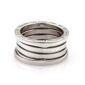 May include: A silver-toned ring with multiple bands stacked together. The ring has a polished finish and a series of engraved letters around the top band. The design is modern and sleek, suitable for everyday wear.