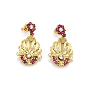 May include: A pair of gold-colored drop earrings. Each earring features a fan-shaped design with a central diamond and surrounding red gemstones. A smaller floral cluster with a diamond center and red gemstones tops each earring.