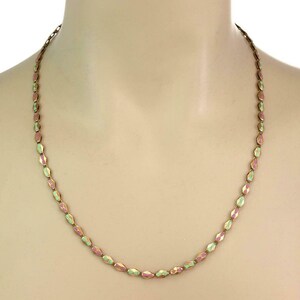 May include: A delicate necklace featuring small, faceted beads in alternating pink and pale green hues. The beads are strung together with a gold-colored chain, creating a subtle, elegant accessory. The necklace is displayed on a mannequin.