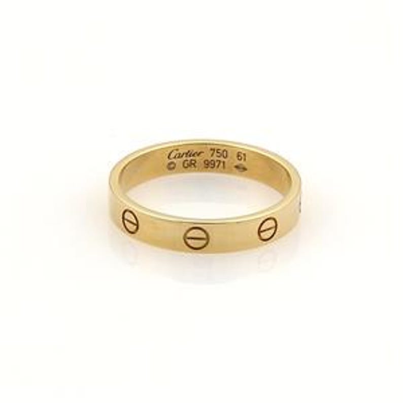 May include: A yellow gold Cartier Love wedding band with screw details. The band is thin and features the iconic Cartier Love collection design.  The inside of the band is engraved with 'Cartier 750 61 © GR 9971'. This luxury wedding band is a classic and timeless piece of jewelry.
