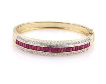 Puede incluir: Un brazalete dorado con una fila central de piedras preciosas rectangulares de color rojo intenso, flanqueada por filas de piedras preciosas redondas y claras. El brazalete tiene un cierre de bisagra y un acabado pulido.