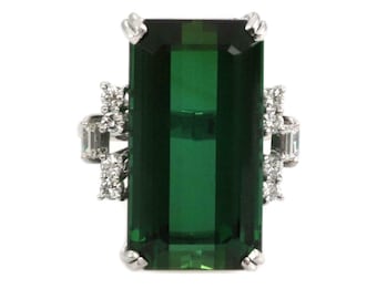 May include: A rectangular emerald-cut green gemstone ring with a white metal setting. The ring features a large, vibrant green center stone, accented by smaller, clear gemstones on the sides. The setting has a detailed, ornate design.