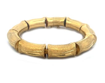 May include: A gold-toned bamboo-style bangle bracelet. The bracelet is made of multiple linked sections that resemble bamboo stalks.