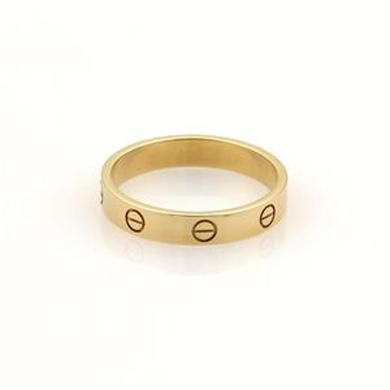 May include: A yellow gold Cartier Love wedding band. The band features a polished finish and is adorned with screw motifs along its surface. This iconic design is a classic symbol of love and commitment. The ring is shown against a plain white background.