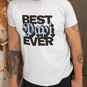 May include: White t-shirt with black text that reads "Best Papi Ever". The word "Papi" is in a light blue color.
