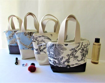 May include: Four small tote bags with cream-colored handles and floral patterns. The bags have a cream-colored base and a black bottom. Accessories like a bottle, lipstick, and a makeup brush are also visible.