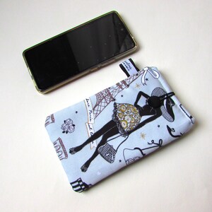 May include: A light blue phone case with a black silhouette of a woman in a hat, Eiffel Tower, and the text "Love Paris". A black smartphone rests above the case. The case has a black tag that says "Idra France".