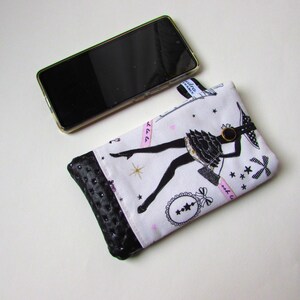 May include: A white and black fabric phone case with a black leather bottom. The case features a black silhouette of a woman in a dress, with pink accents and text. A black smartphone is next to the case.