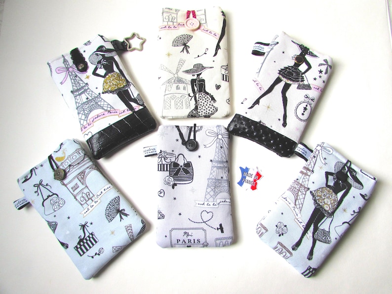 May include: A collection of fabric phone cases with Parisian-themed designs. The cases feature illustrations of the Eiffel Tower, fashion figures, and other Parisian motifs in black and white, with accents of gold and black. Each case has a black leather-like bottom.