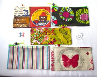May include: Collection of colorful zippered pouches with various designs. One pouch features a vintage coffee advertisement, another has a floral pattern, and a third displays a butterfly. The pouches have different colored zippers.
