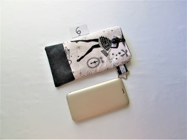 May include: A black and white patterned phone case with a black leather accent, a star-shaped charm, and a gold-colored smartphone. The case features a ballerina design and the number 6.