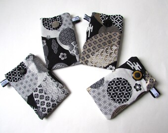 May include: Four small, rectangular fabric pouches with Japanese-inspired patterns in black, white, and gray. Each pouch has a button closure and a small fabric loop with text. The pouches are arranged on a white surface.