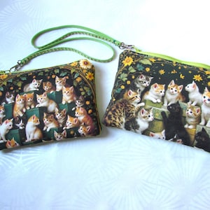 Può includere: Due pochette rettangolari con cerniera e motivo a gatti. Le pochette presentano uno sfondo nero con una stampa di numerosi gattini in vari colori. Le pochette hanno una cerniera verde e un cinturino verde.