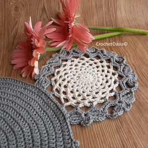 May include: Two crocheted doilies, one gray and one white with a gray border, on a wood surface with pink flowers.